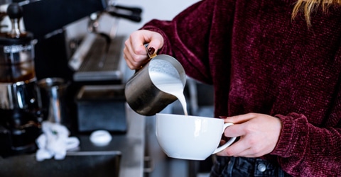 person pouring steamed milk into a mug